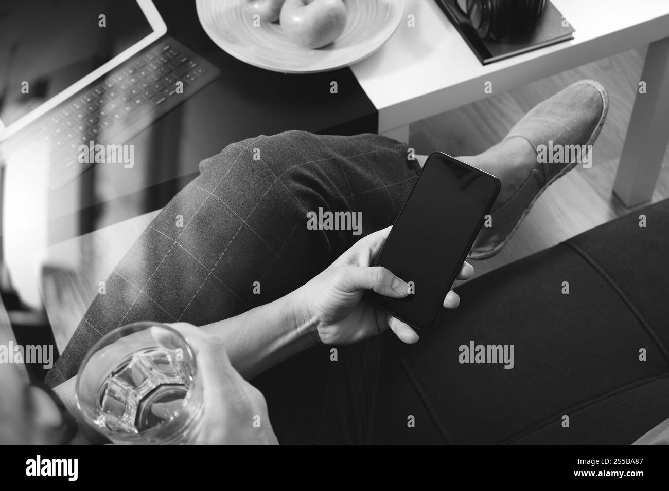main hipster utilisant un téléphone intelligent pour les paiements mobiles en ligne, verre d'eau, assis sur un canapé dans le salon, pommes vertes dans un plateau en bois, noir Banque D'Images