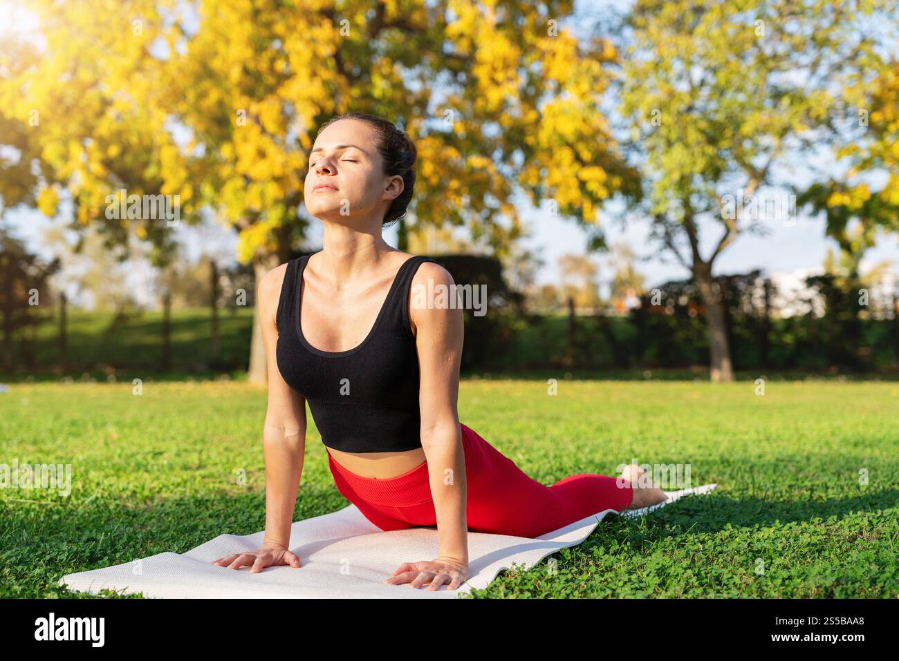 Femme caucasienne pratiquant le yoga sur un tapis dans un parc de la ville. Yoga matinal. Banque D'Images