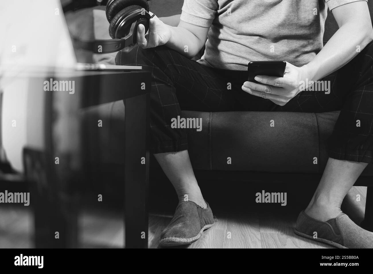 main hipster utilisant le téléphone intelligent pour les paiements mobiles en ligne affaires, casque, assis sur le canapé dans le salon, noir et blanc Banque D'Images