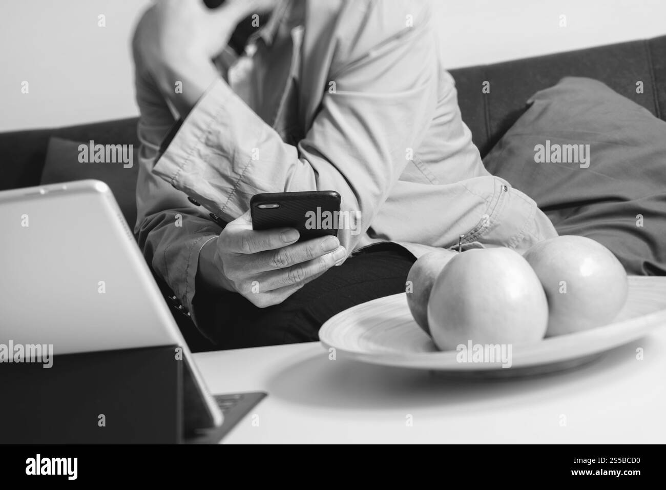 main hipster utilisant le téléphone intelligent pour les paiements mobiles en ligne, assis sur le canapé dans le salon, tenant la pomme verte dans le plateau en bois, noir et blanc Banque D'Images