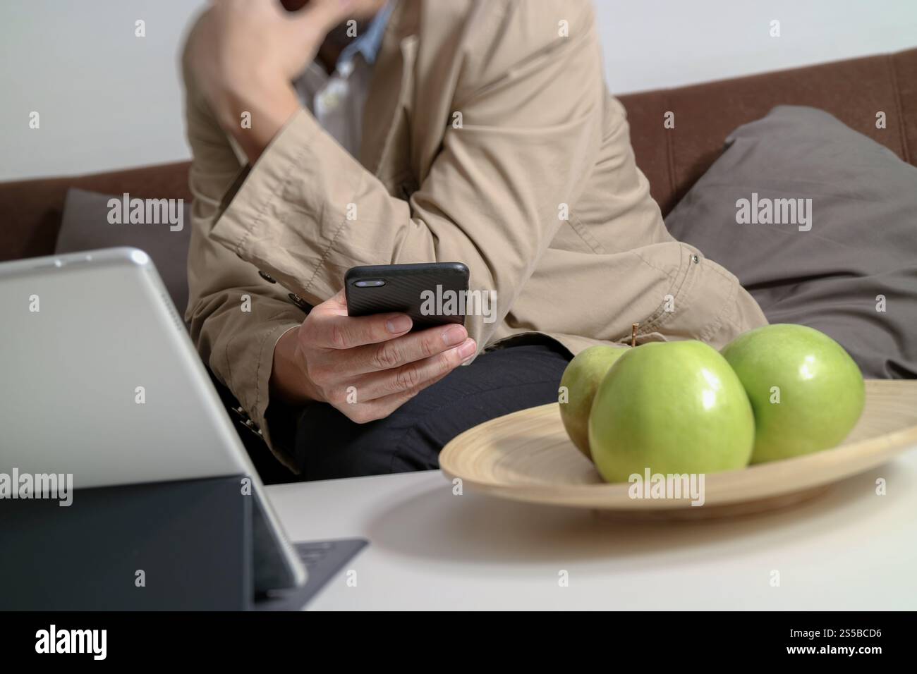 Hipster la main à l'aide de smart phone pour les paiements mobiles les entreprises en ligne, sitting on sofa in living room,holding green apple en plateau en bois Banque D'Images