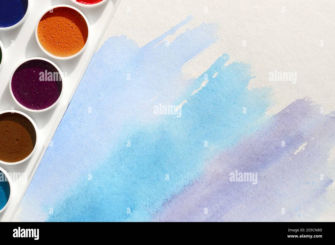 Un nouvel ensemble d'aquarelles repose sur une feuille de papier, qui montre un dessin abstrait d'aquarelle sous la forme de traits bleus. Le concept d'amateur Banque D'Images