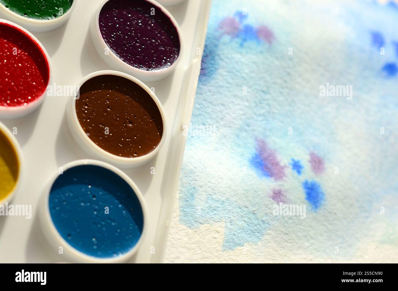 Un nouvel ensemble d'aquarelles repose sur une feuille de papier, qui montre un dessin abstrait d'aquarelle sous la forme de traits bleus. Le concept d'amateur Banque D'Images