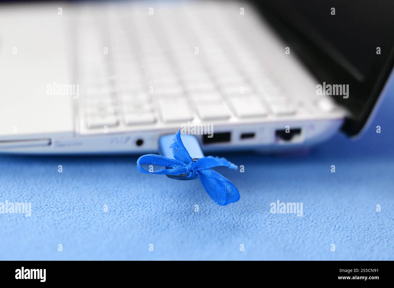 Le bleu brillant d'un lecteur flash USB avec un blue bow est connecté à un ordinateur portable blanc, qui se trouve sur une couverture douce et moelleuse de tissu polaire bleu clair. Banque D'Images