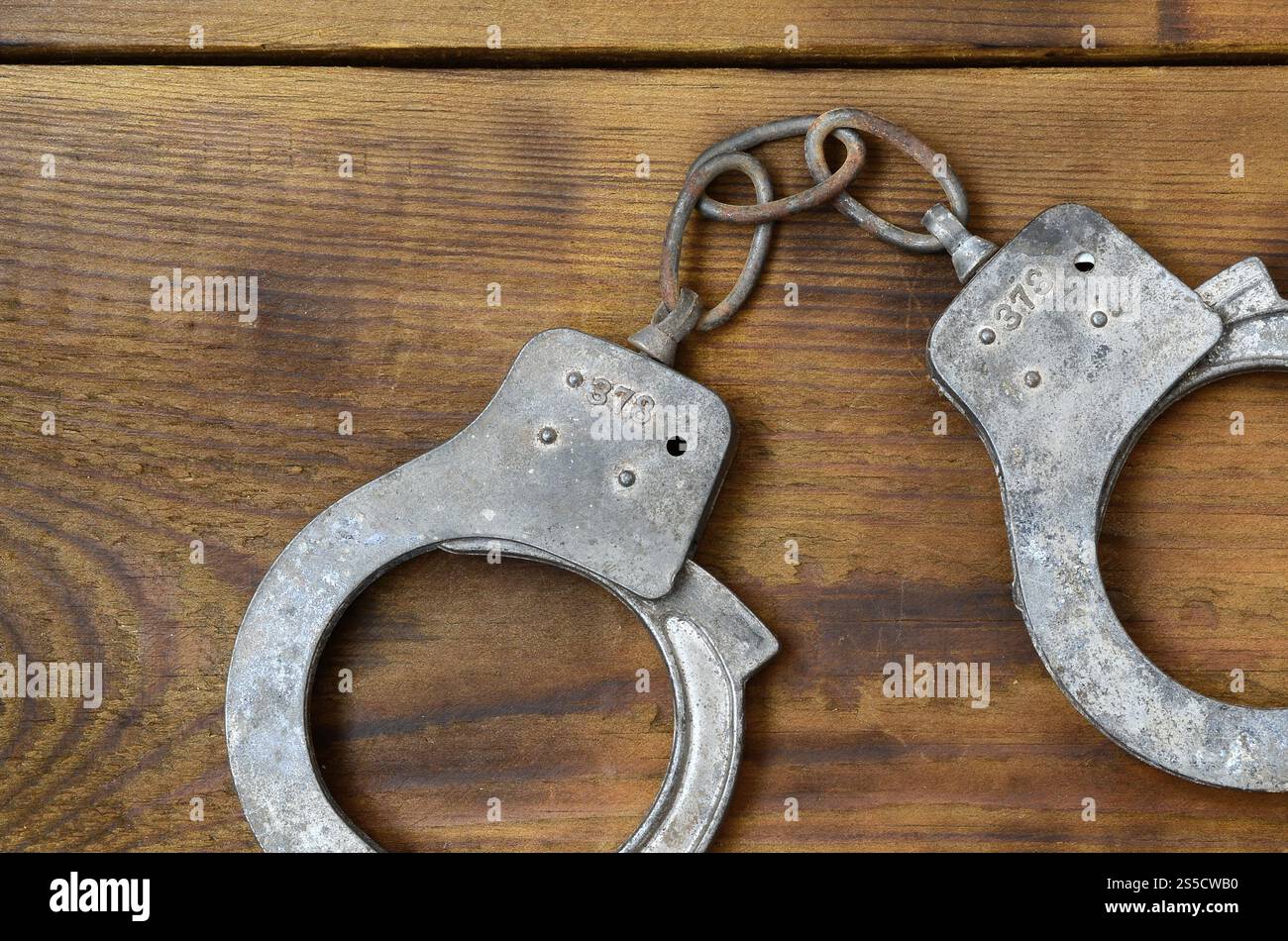 Les menottes de police vieilles et rouillées reposent sur une surface en bois rayée. Le concept d'un vieux crime Banque D'Images
