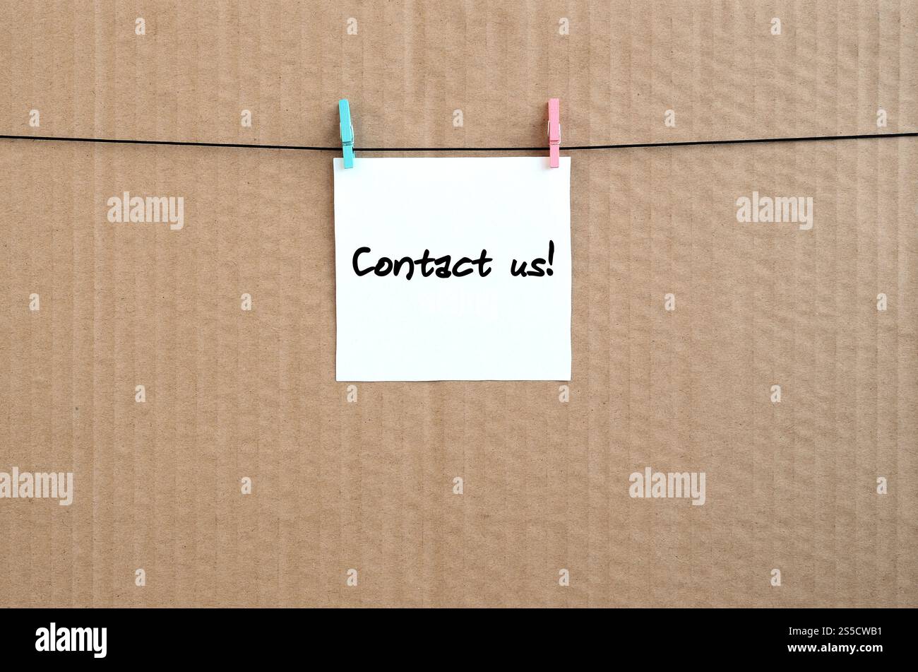 Contactez-nous ! La note est écrite sur un autocollant blanc qui est suspendu avec une épingle à linge sur une corde sur un fond de carton brun Banque D'Images