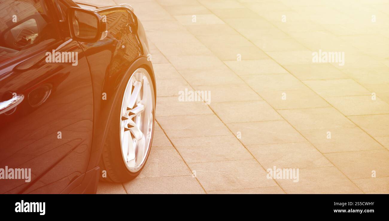 Vue en diagonale d'une voiture noire brillante avec des roues blanches, qui se trouve sur un carré de carreaux gris Banque D'Images