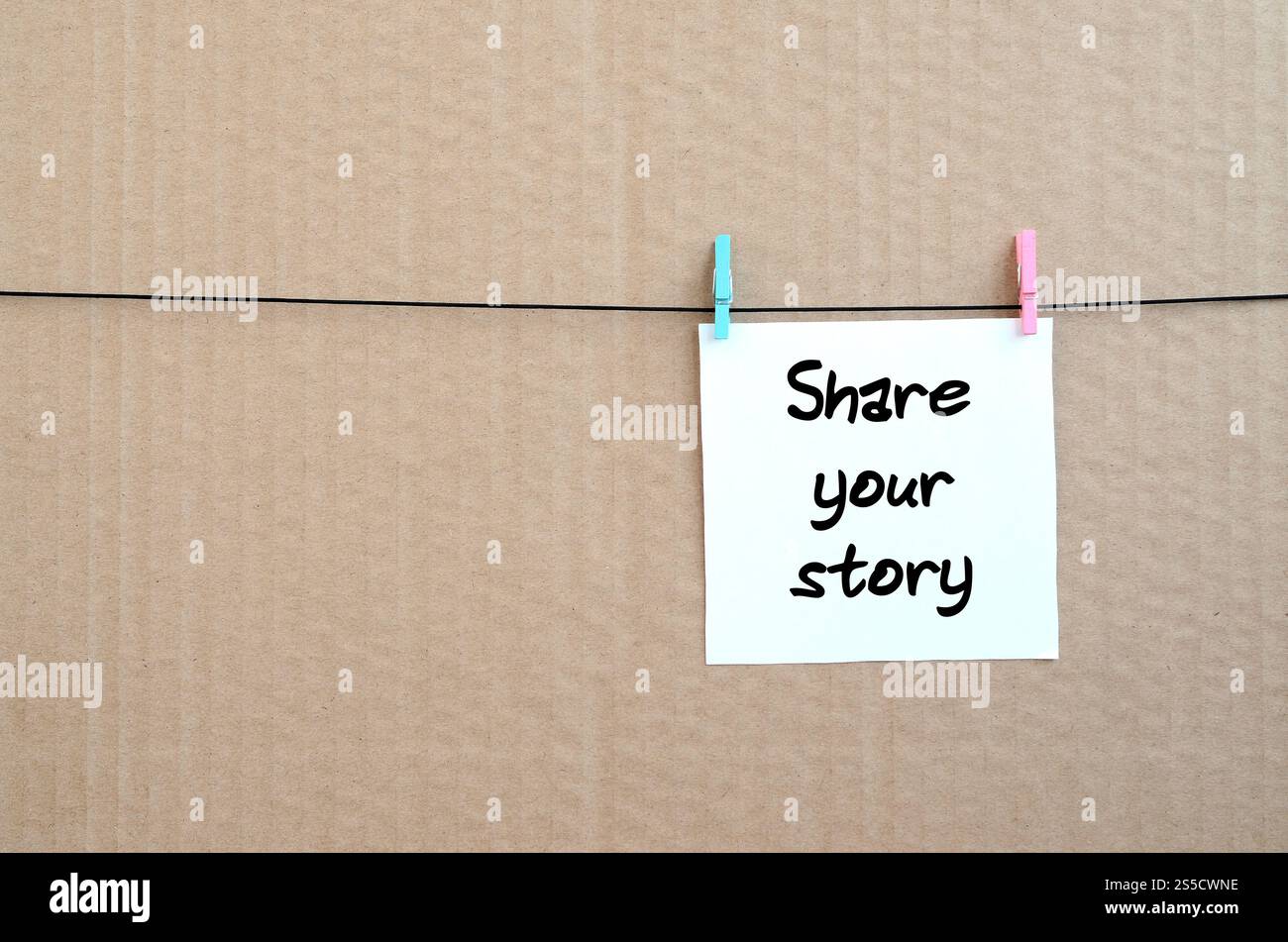 Partagez votre histoire. La note est écrite sur un autocollant blanc qui est suspendu avec une épingle à linge sur une corde sur un fond de carton brun Banque D'Images