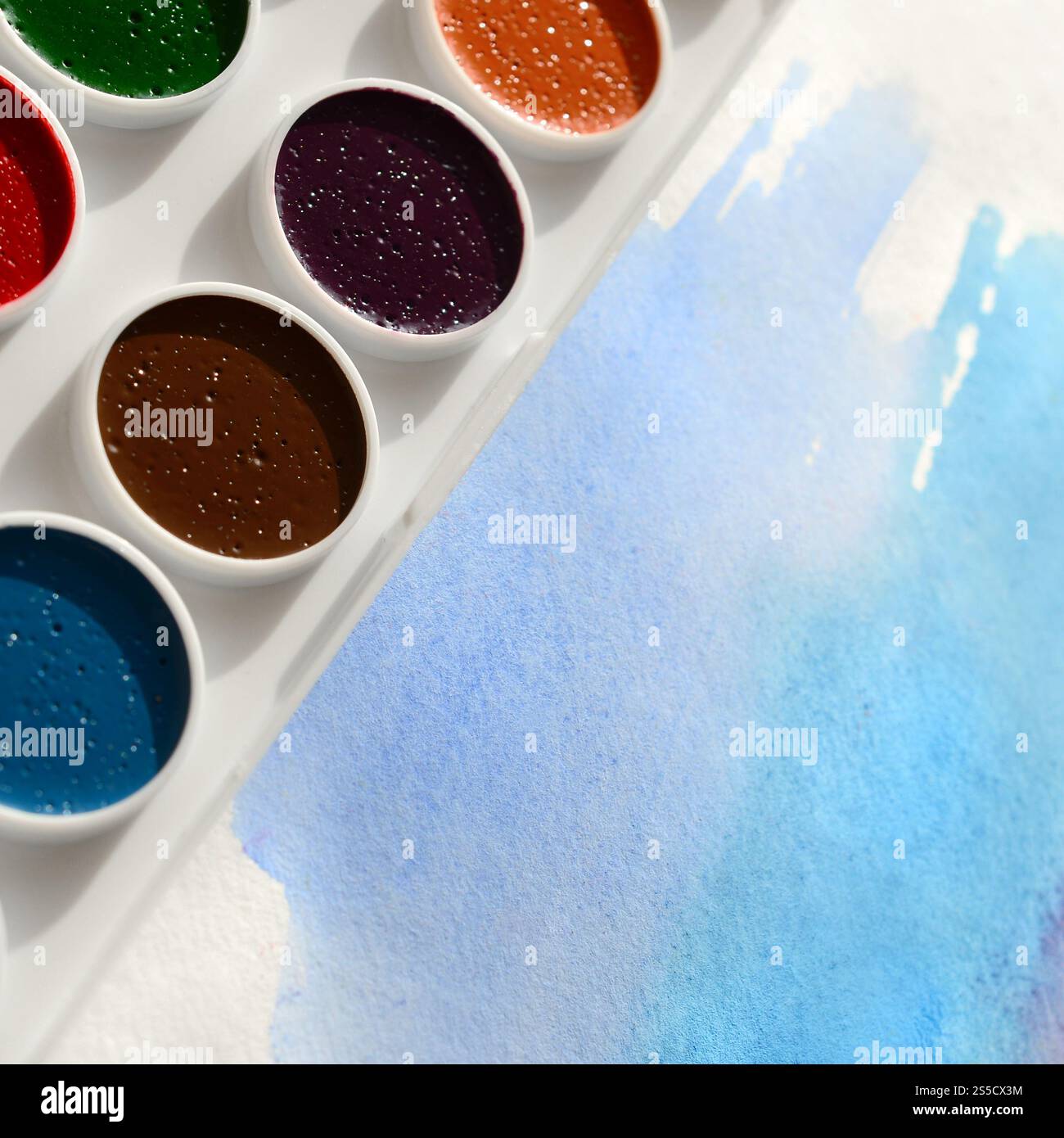 Un nouvel ensemble d'aquarelles repose sur une feuille de papier, qui montre un dessin abstrait d'aquarelle sous la forme de traits bleus. Le concept d'amateur Banque D'Images