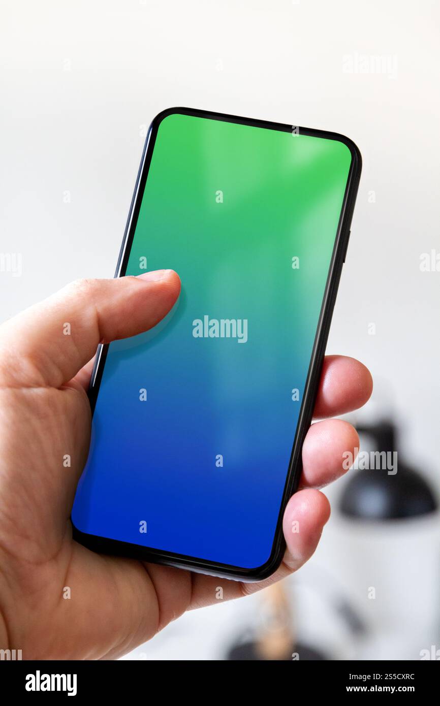 Main tenant un smartphone avec un écran bleu et vert vierge. Fond blanc de bureau. Main tenant un smartphone avec un écran bleu et vert vierge. Banque D'Images