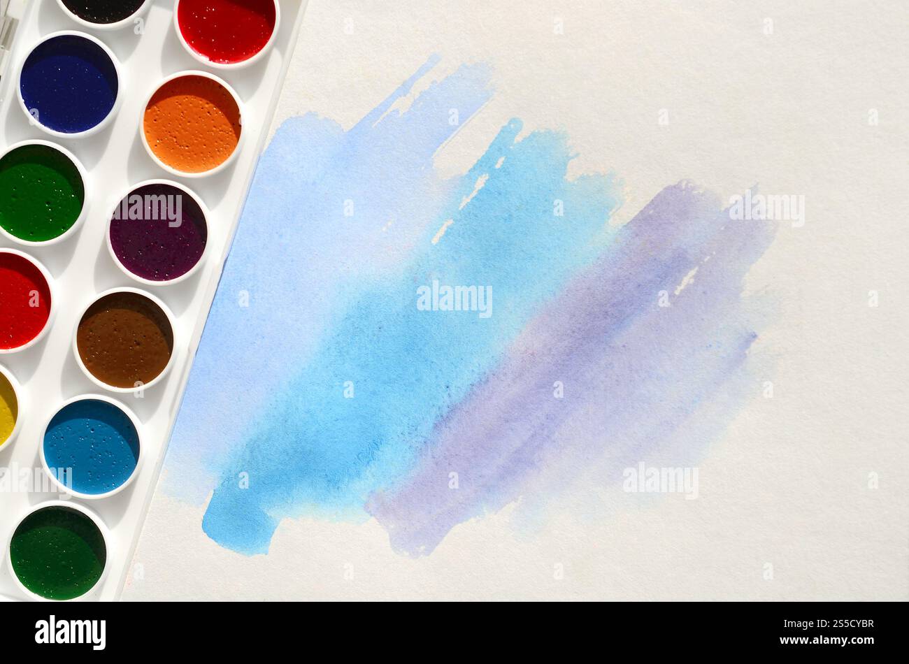 Un nouvel ensemble d'aquarelles repose sur une feuille de papier, qui montre un dessin abstrait d'aquarelle sous la forme de traits bleus. Le concept d'amateur Banque D'Images