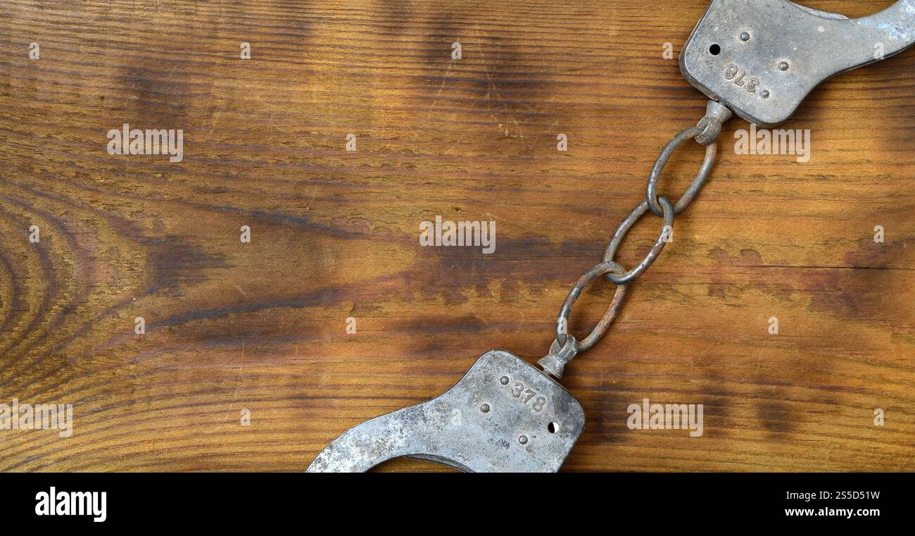 Les menottes de police vieilles et rouillées reposent sur une surface en bois rayée. Le concept d'un vieux crime Banque D'Images
