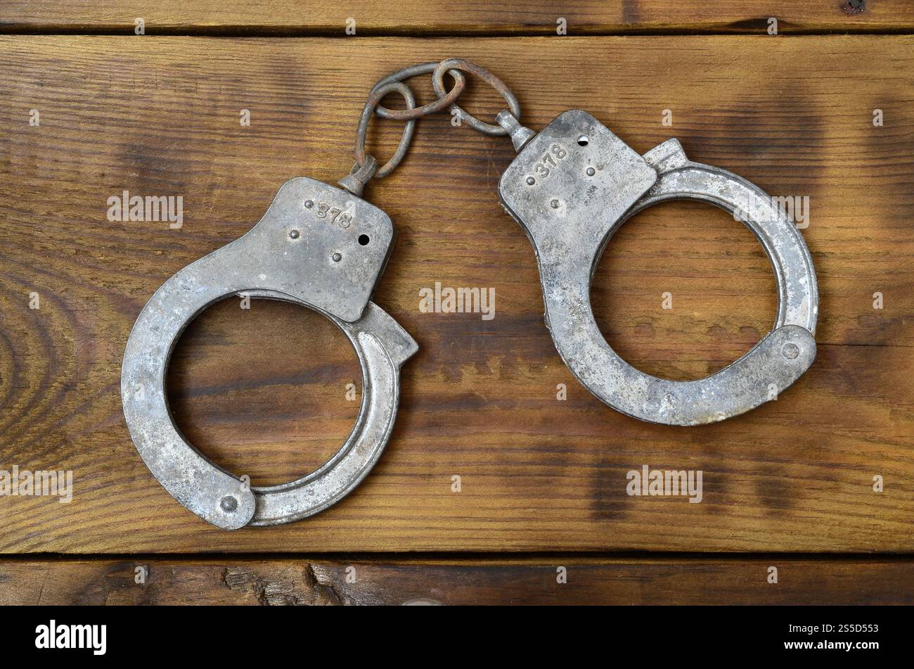 Les menottes de police vieilles et rouillées reposent sur une surface en bois rayée. Le concept d'un vieux crime Banque D'Images