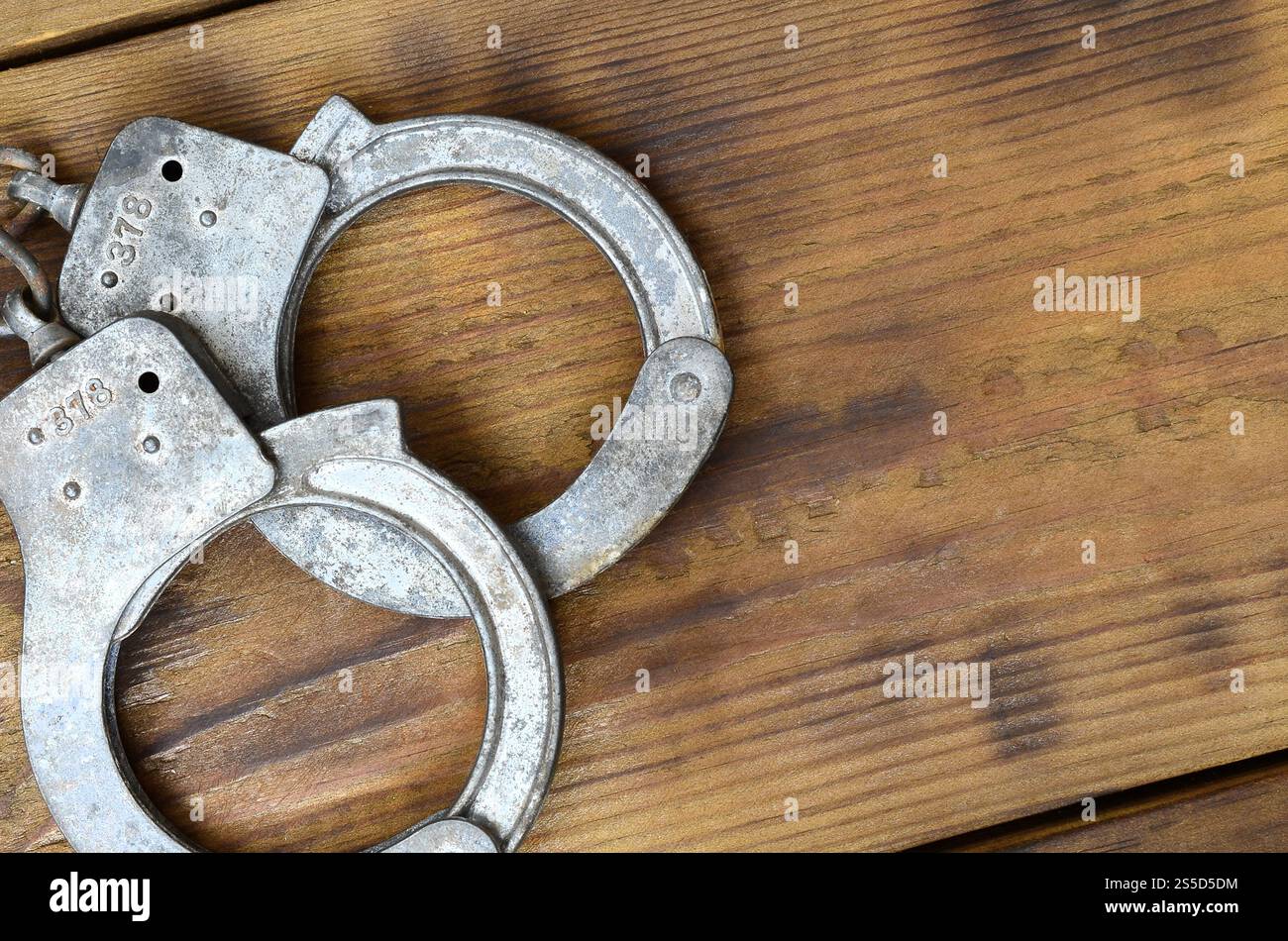Les menottes de police vieilles et rouillées reposent sur une surface en bois rayée. Le concept d'un vieux crime Banque D'Images