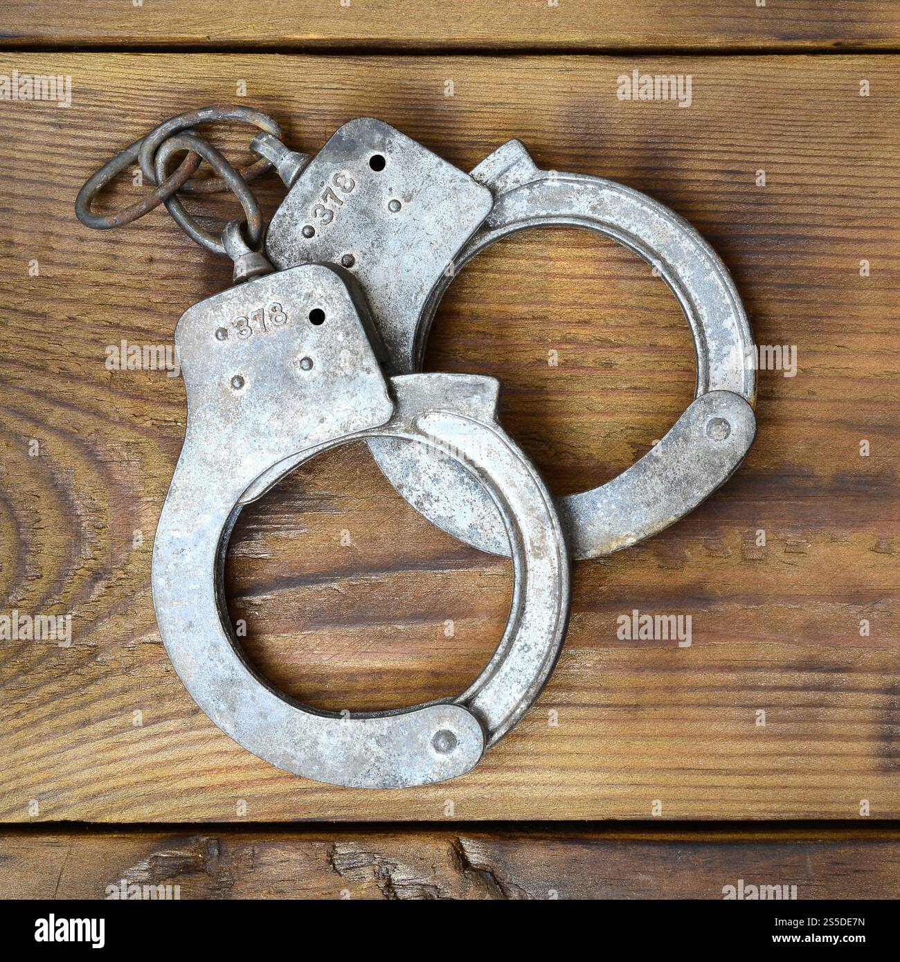 Les menottes de police vieilles et rouillées reposent sur une surface en bois rayée. Le concept d'un vieux crime Banque D'Images