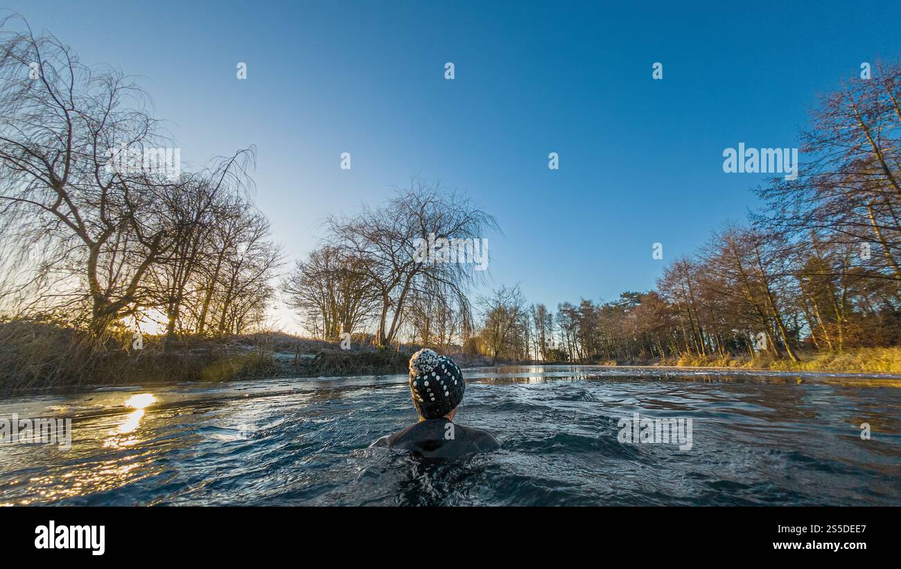 Baignade sauvage en hiver. Un nageur solitaire portant un chapeau grise nageant dans l'eau glacée loin de la caméra. Banque D'Images
