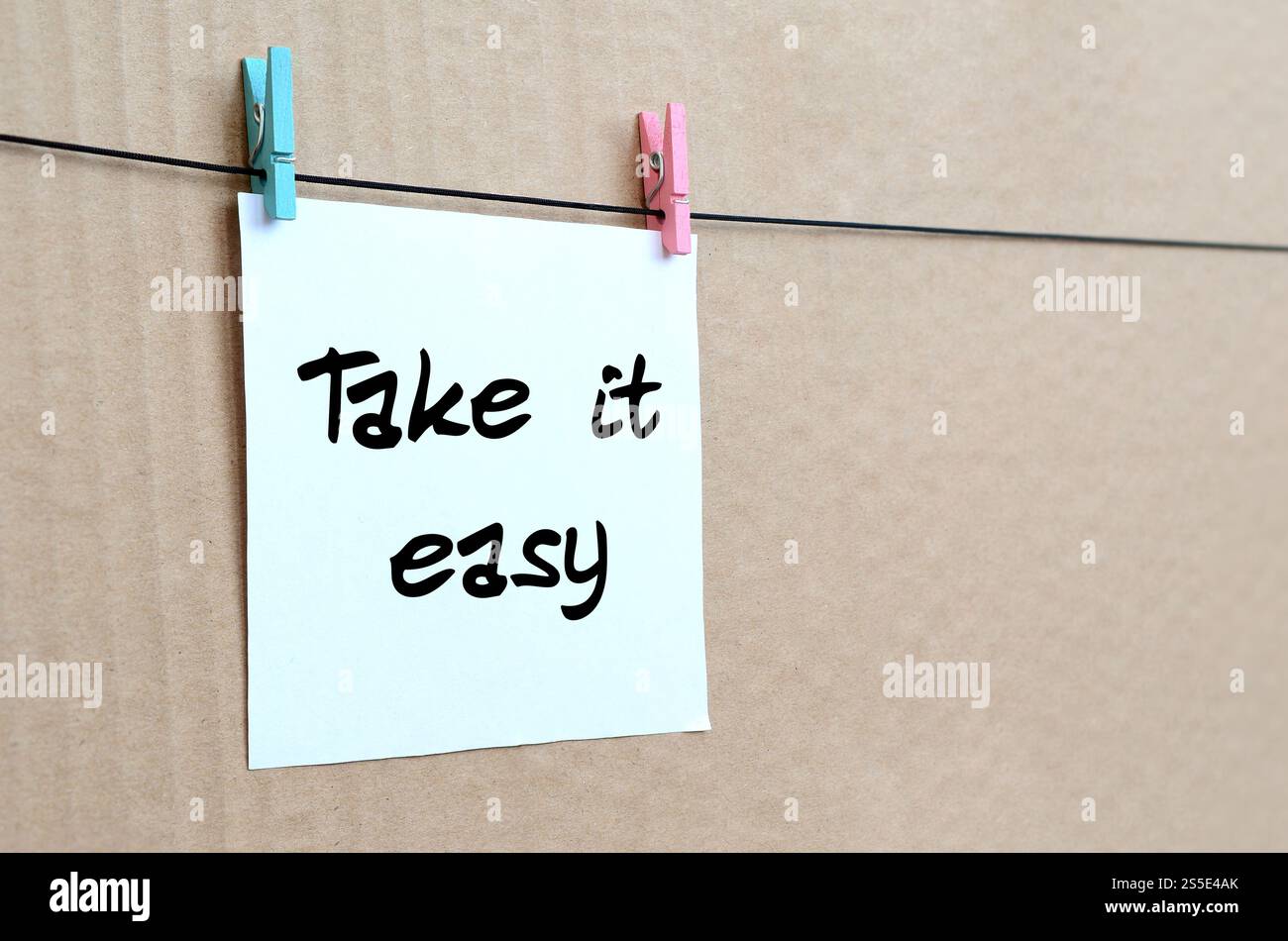 Détendez-vous. Note est écrit sur un autocollant blanc qui est suspendu avec une pince à linge sur une corde sur un fond de carton brun Banque D'Images