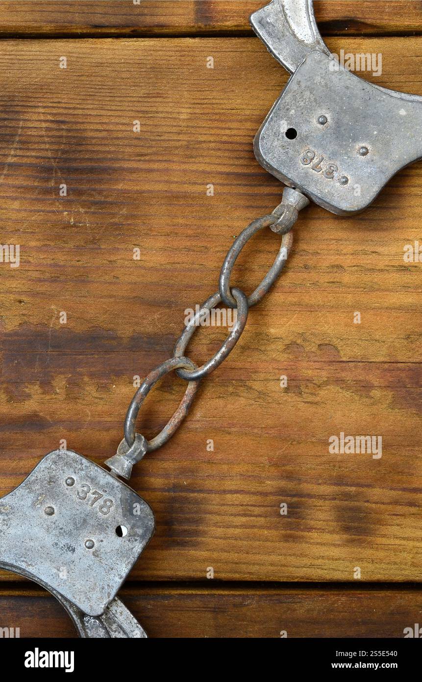 Les menottes de police vieilles et rouillées reposent sur une surface en bois rayée. Le concept d'un vieux crime Banque D'Images
