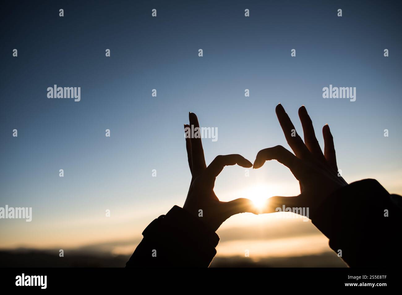 Silhouette des mains formant un coeur avec le lever du soleil Banque D'Images