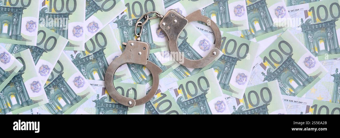 Les menottes de police se trouvent sur un ensemble de coupures monétaires vertes de 100 euros. Beaucoup d'argent forme un tas infini Banque D'Images