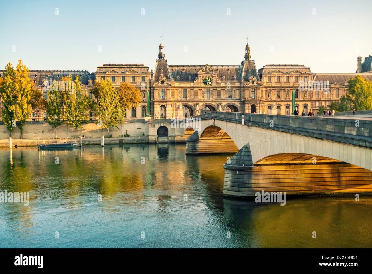 Élégant bâtiment historique du Musée du Louvre et pont sur une Seine calme au coucher du soleil, avec un ciel clair et une lumière chaude baignant la scène, Paris, France Banque D'Images