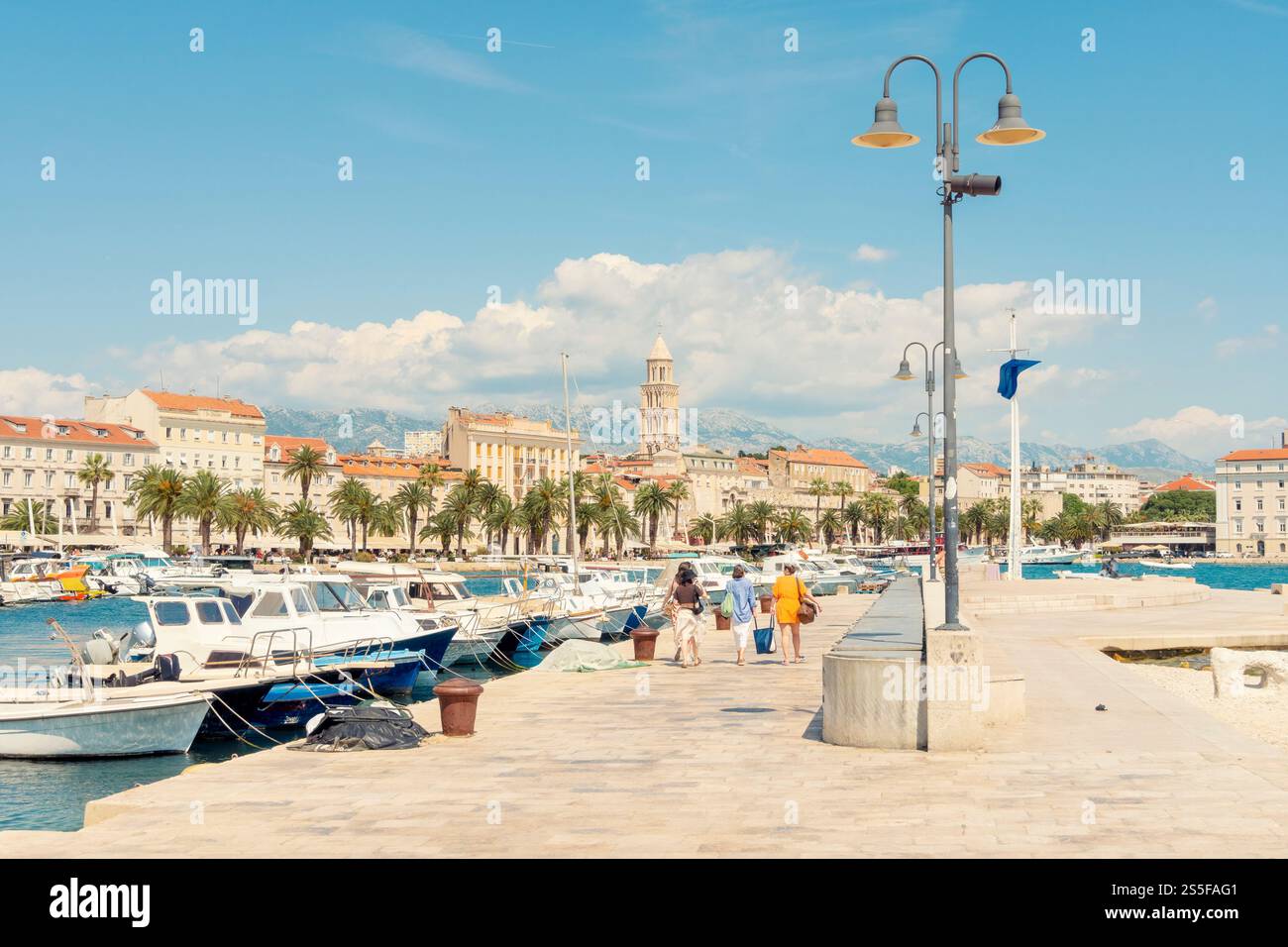Journée ensoleillée dans une marina méditerranéenne avec des bateaux amarrés, des gens qui se promènent, et des bâtiments historiques en arrière-plan, Split, Croatie. Banque D'Images
