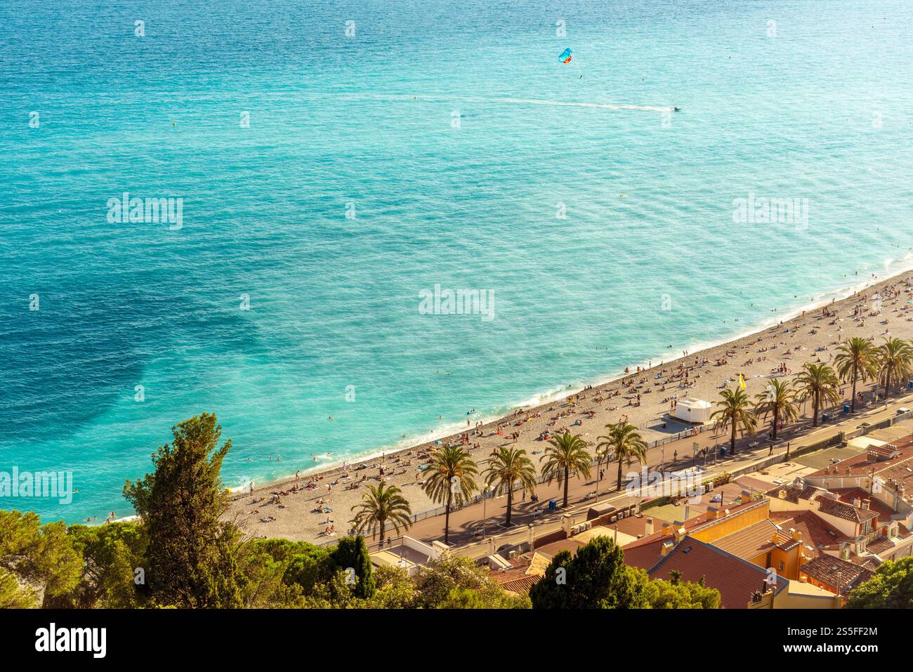 Vue imprenable sur la plage animée de la ville de Nice sur la côte d'azur avec des bains de soleil, un parachute ascensionnel au loin et des eaux turquoises cristallines. Banque D'Images