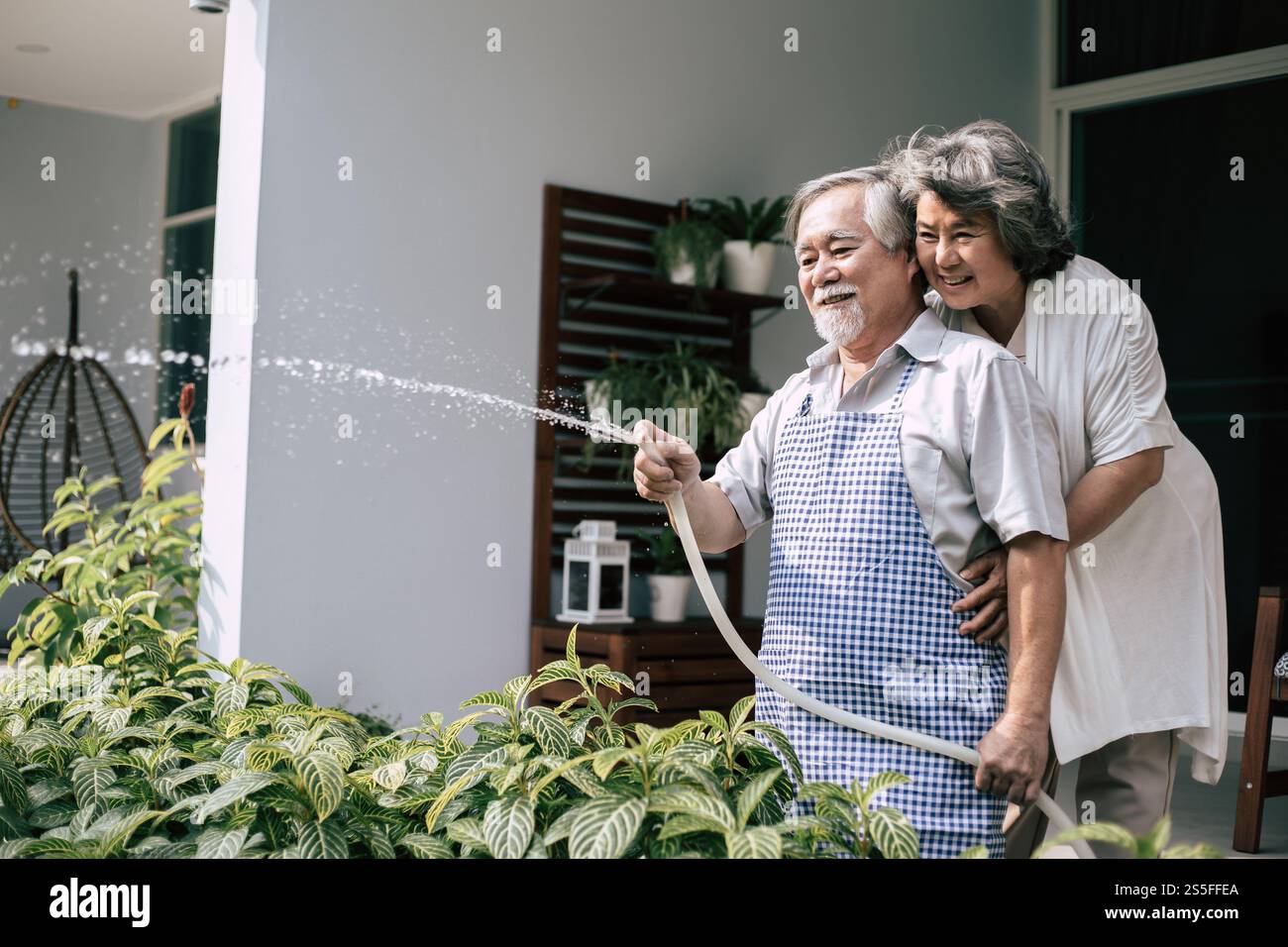 Couple âgé arrosant une fleur dans le jardin de la maison Banque D'Images