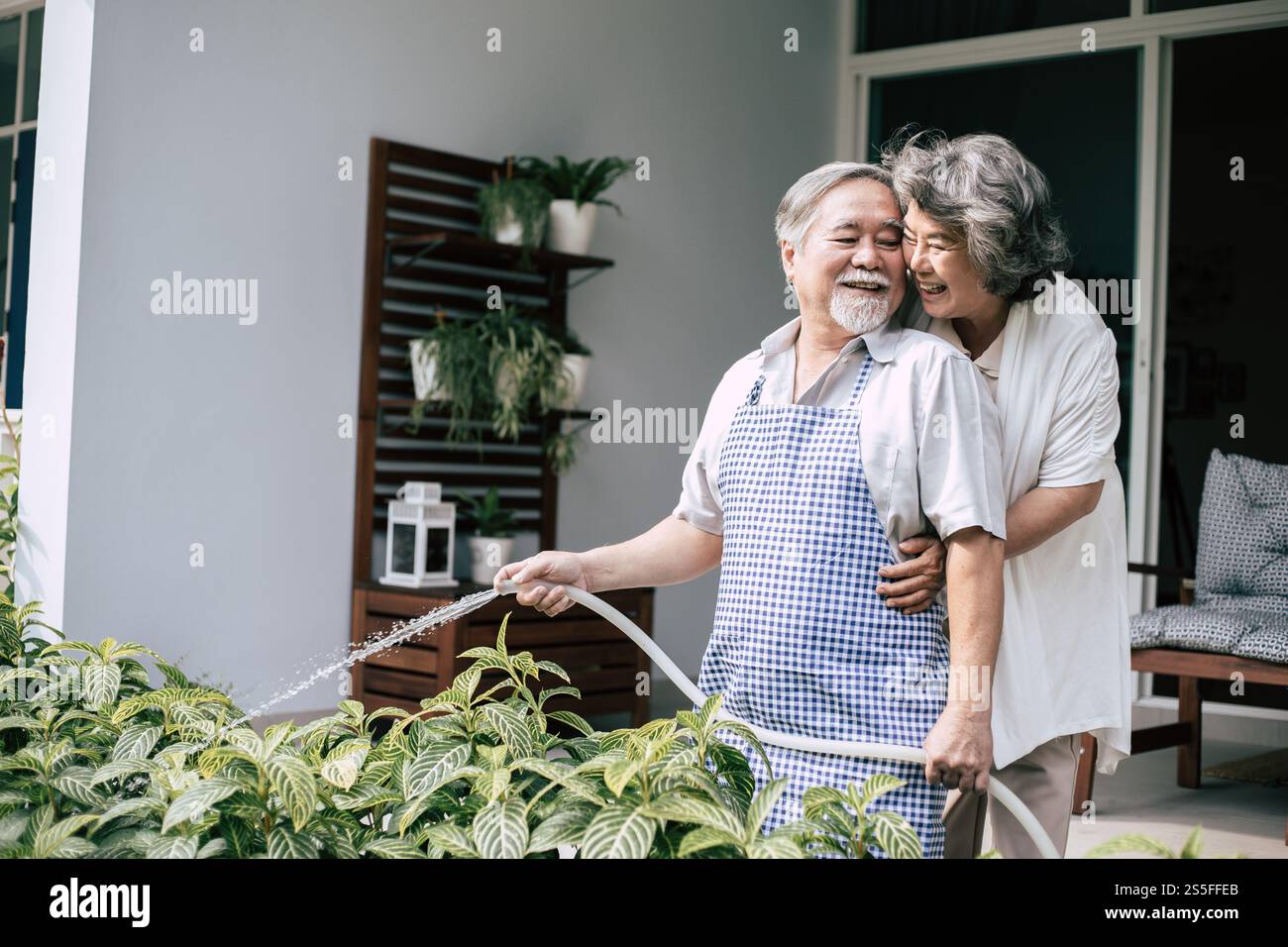 Couple âgé arrosant une fleur dans le jardin de la maison Banque D'Images