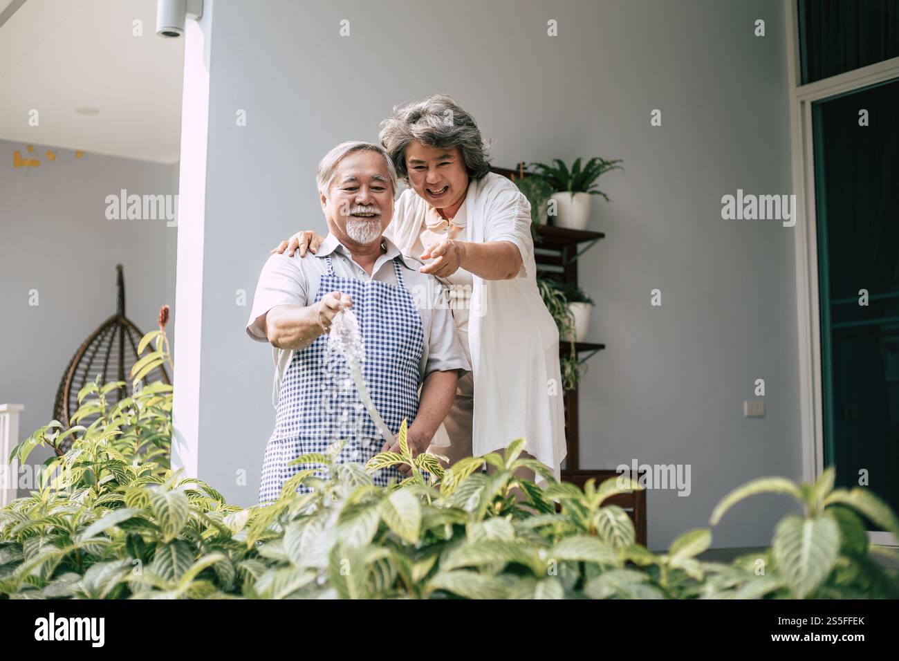 Couple âgé arrosant une fleur dans le jardin de la maison Banque D'Images
