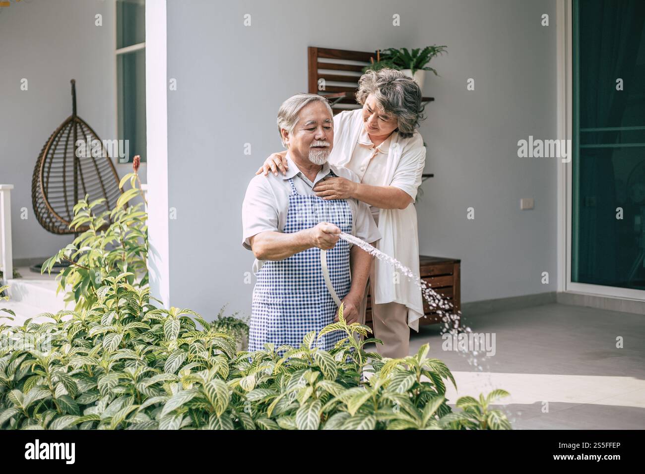 Couple âgé arrosant une fleur dans le jardin de la maison Banque D'Images