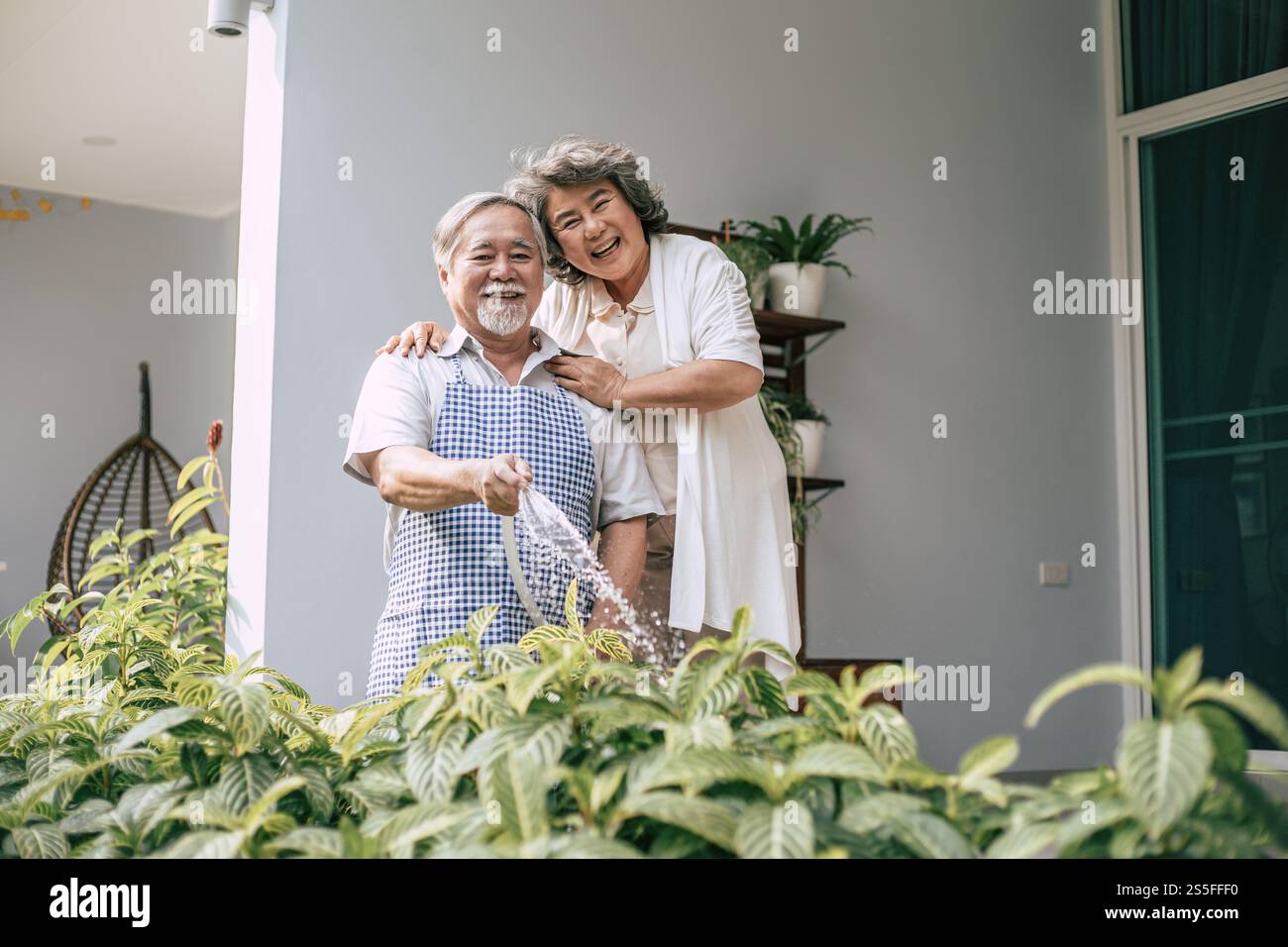 Couple âgé arrosant une fleur dans le jardin de la maison Banque D'Images