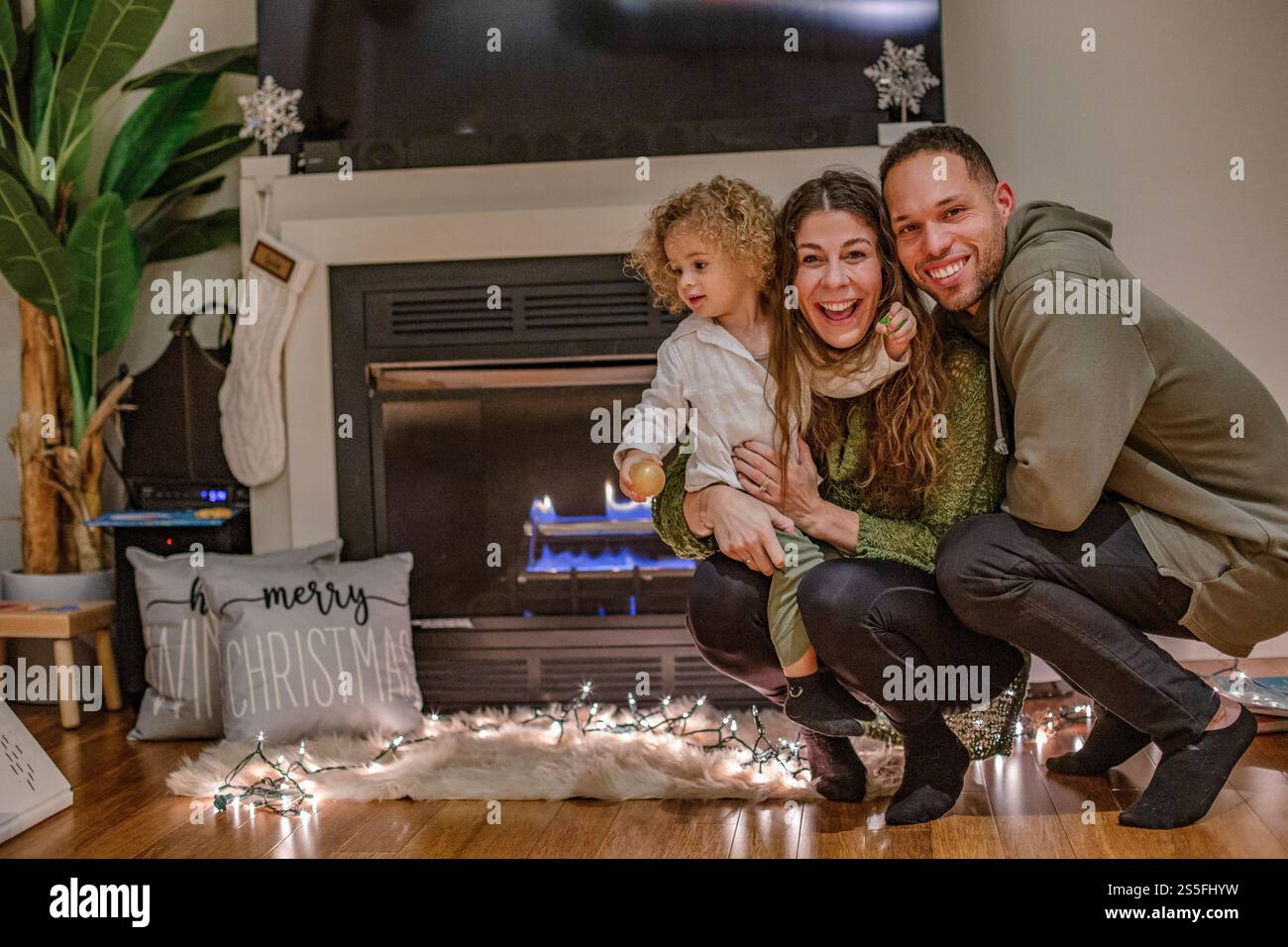 La famille profite des festivités de Noël près de la cheminée, avec des lumières festives et des décorations de vacances autour, Ohio, États-Unis Banque D'Images