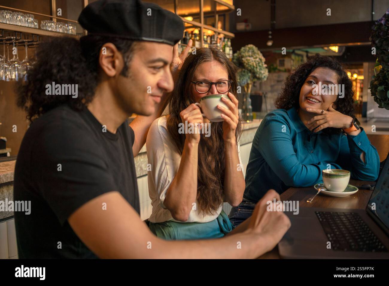 Trois amis profitent d'une conversation autour d'un café-bar confortable, travaillant sur un ordinateur portable, Berlin, Allemagne Banque D'Images