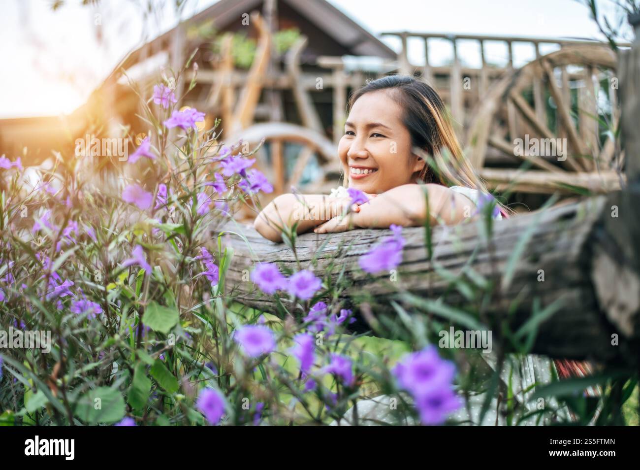 La femme s'est assise joyeusement dans le jardin fleuri et a posé ses mains et vers la clôture en bois. Banque D'Images