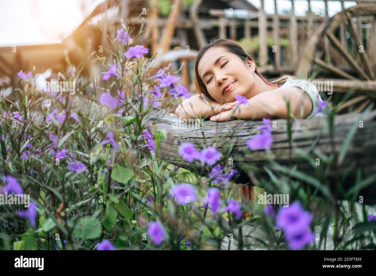 La femme s'est assise joyeusement dans le jardin fleuri et a posé ses mains et vers la clôture en bois. Banque D'Images