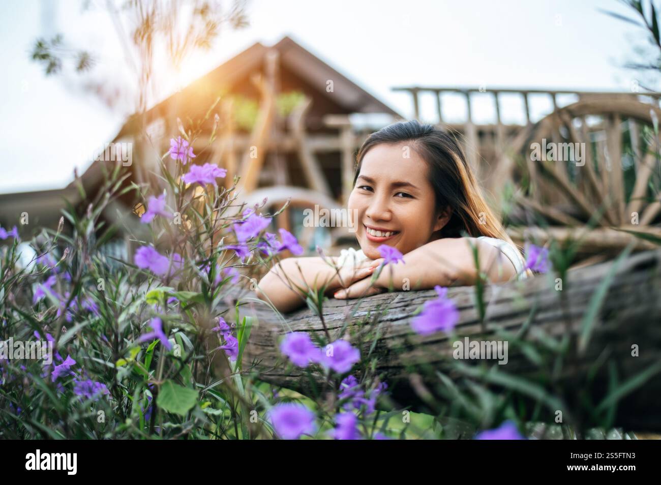 La femme s'est assise joyeusement dans le jardin fleuri et a posé ses mains et vers la clôture en bois. Banque D'Images