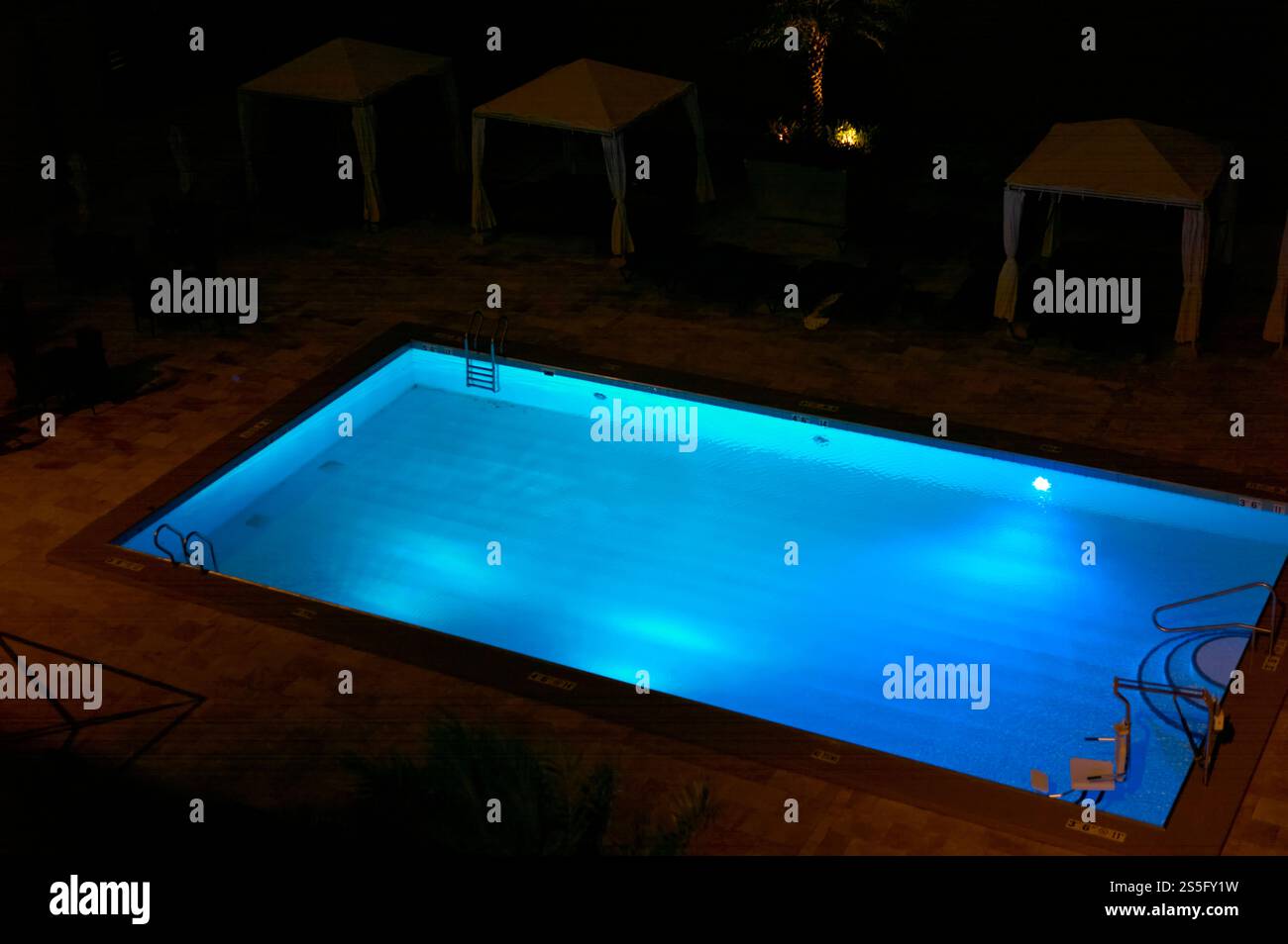 Piscine extérieure éclairée la nuit entourée de cabines et de chaises longues, Nouvelle-Orléans, États-Unis Banque D'Images