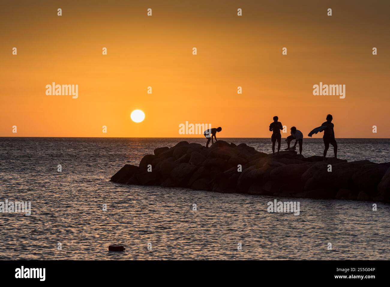 Quatre jeunes silhouettes profitent d'un coucher de soleil sur une île tropicale sur un éperon rocheux Banque D'Images