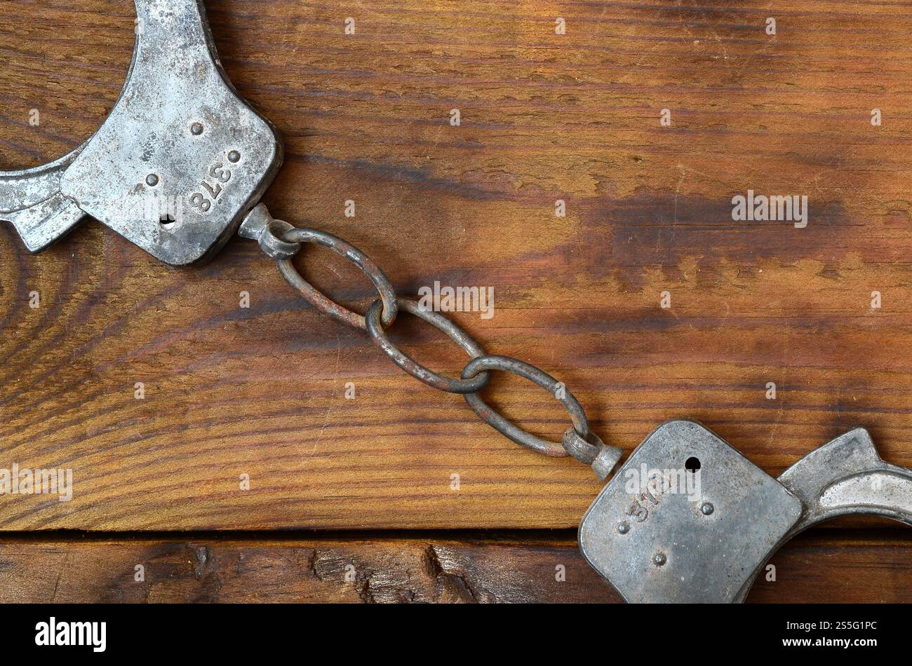 Les menottes de police vieilles et rouillées reposent sur une surface en bois rayée. Le concept d'un vieux crime Banque D'Images