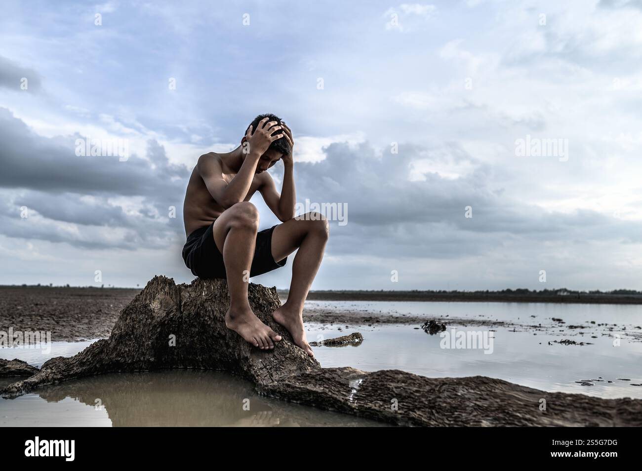 Un homme s'assit les genoux et mit ses mains sur sa tête, sur la base de l'arbre et entouré d'eau. Banque D'Images
