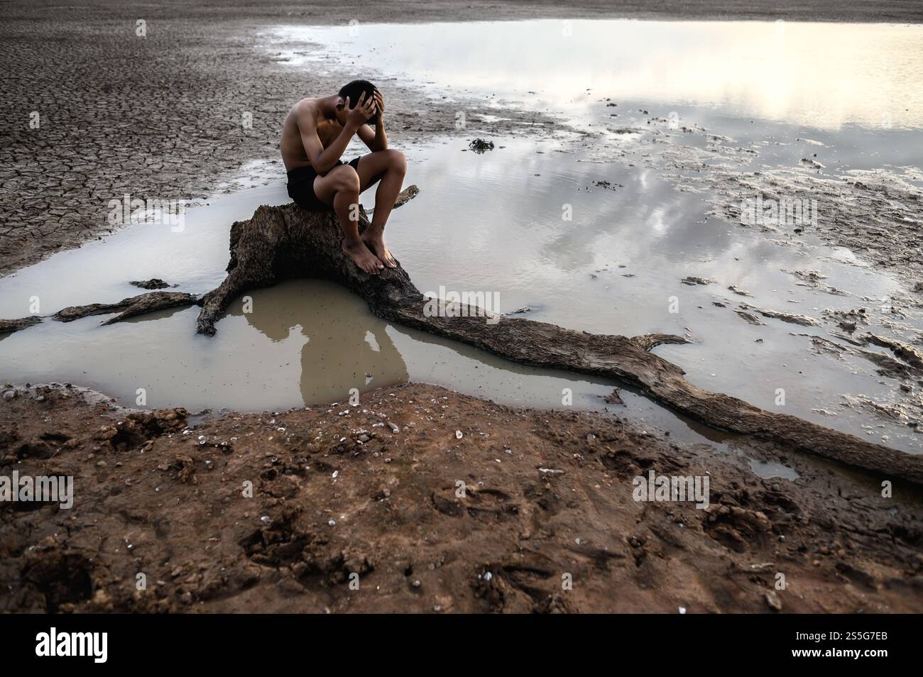 Un homme s'assit les genoux et mit ses mains sur sa tête, sur la base de l'arbre et entouré d'eau. Banque D'Images