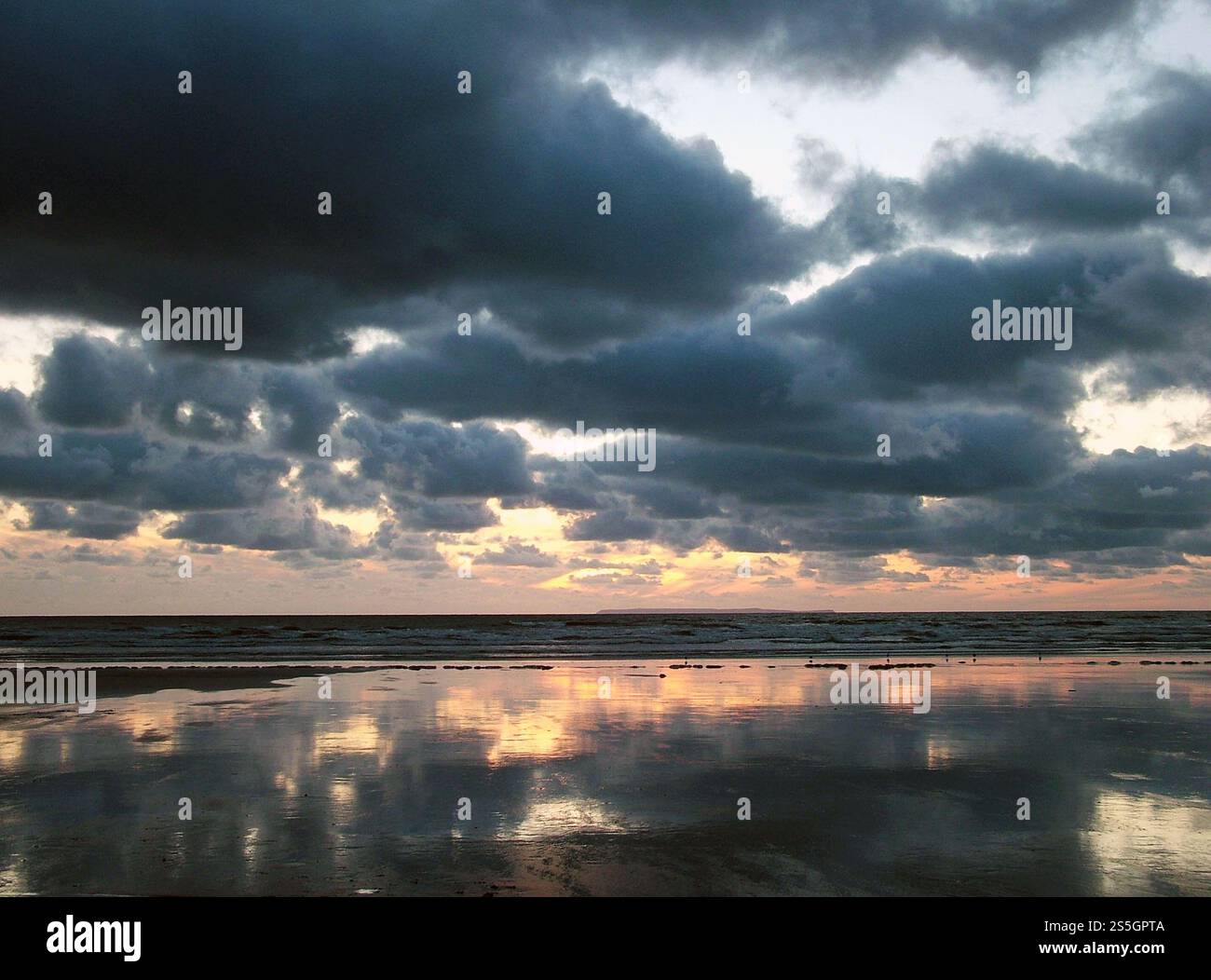 Le coucher du soleil se reflétait dans le sable humide au-dessus de l'île lointaine de Lundy sous un ciel descendant et une mer calme au large des Burrows de Braunton dans le Devon du Nord. Banque D'Images