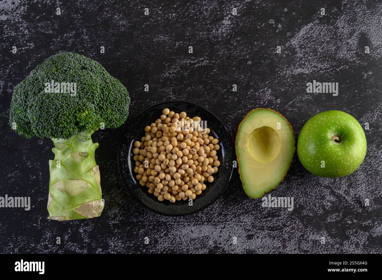 Brocoli, fèves de soja, pomme et avocat sur un fond de sol en ciment noir. Banque D'Images
