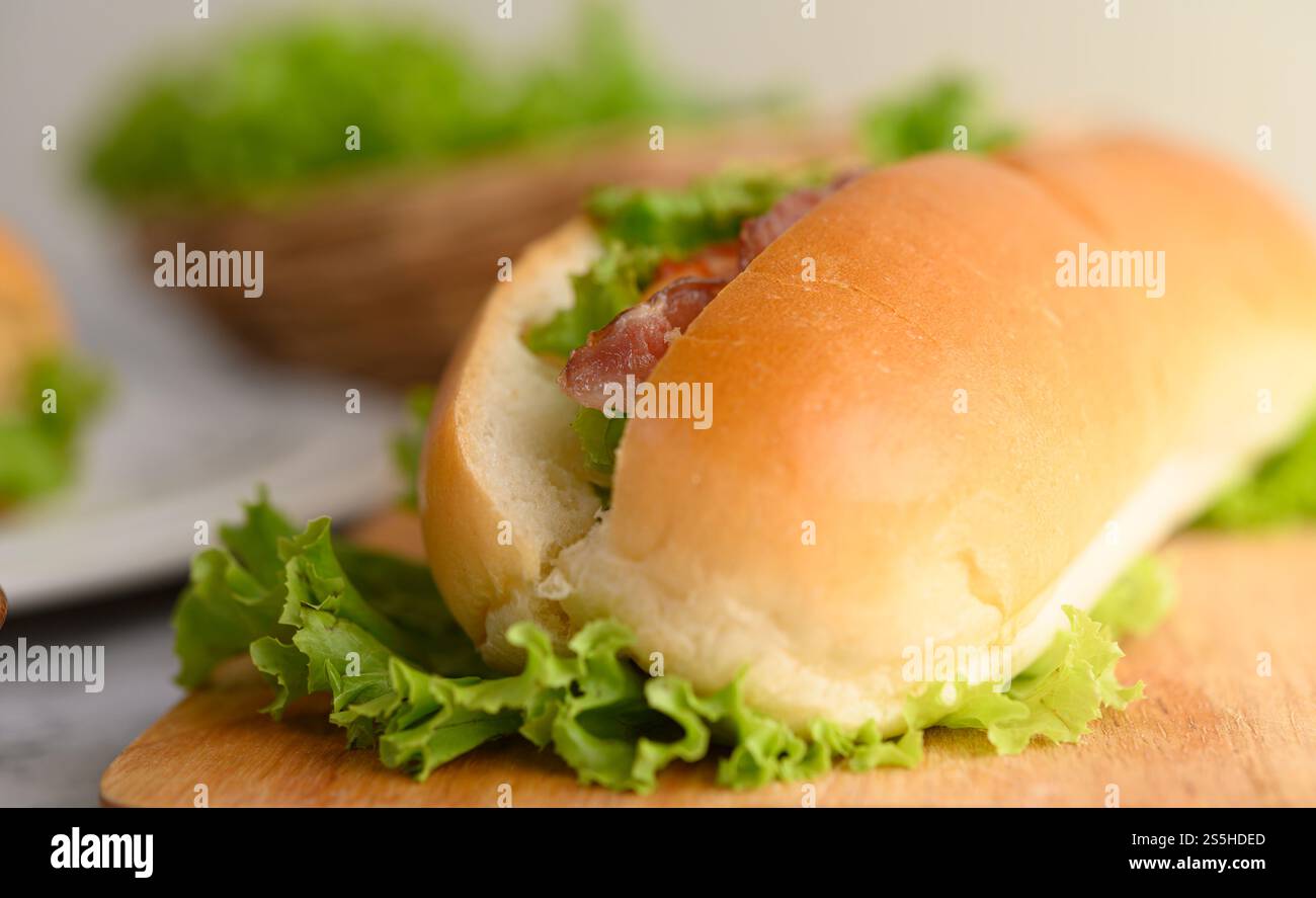 Mise au point sélective et gros plan du pain hotdog avec bacon et laitue sur une planche à découper en bois, espace de copie Banque D'Images Mise au point sélective et gros plan du pain hotdog avec bacon et laitue sur une planche à découper en bois, espace de copie Banque D'Images