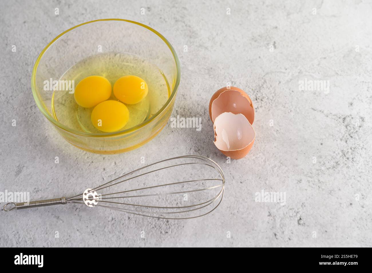 Trois de jaune dans des verres bol et coquille d'oeuf et fouet sur le sol, la préparation pour la cuisson des aliments ou dessert, copier l'espace Banque D'Images