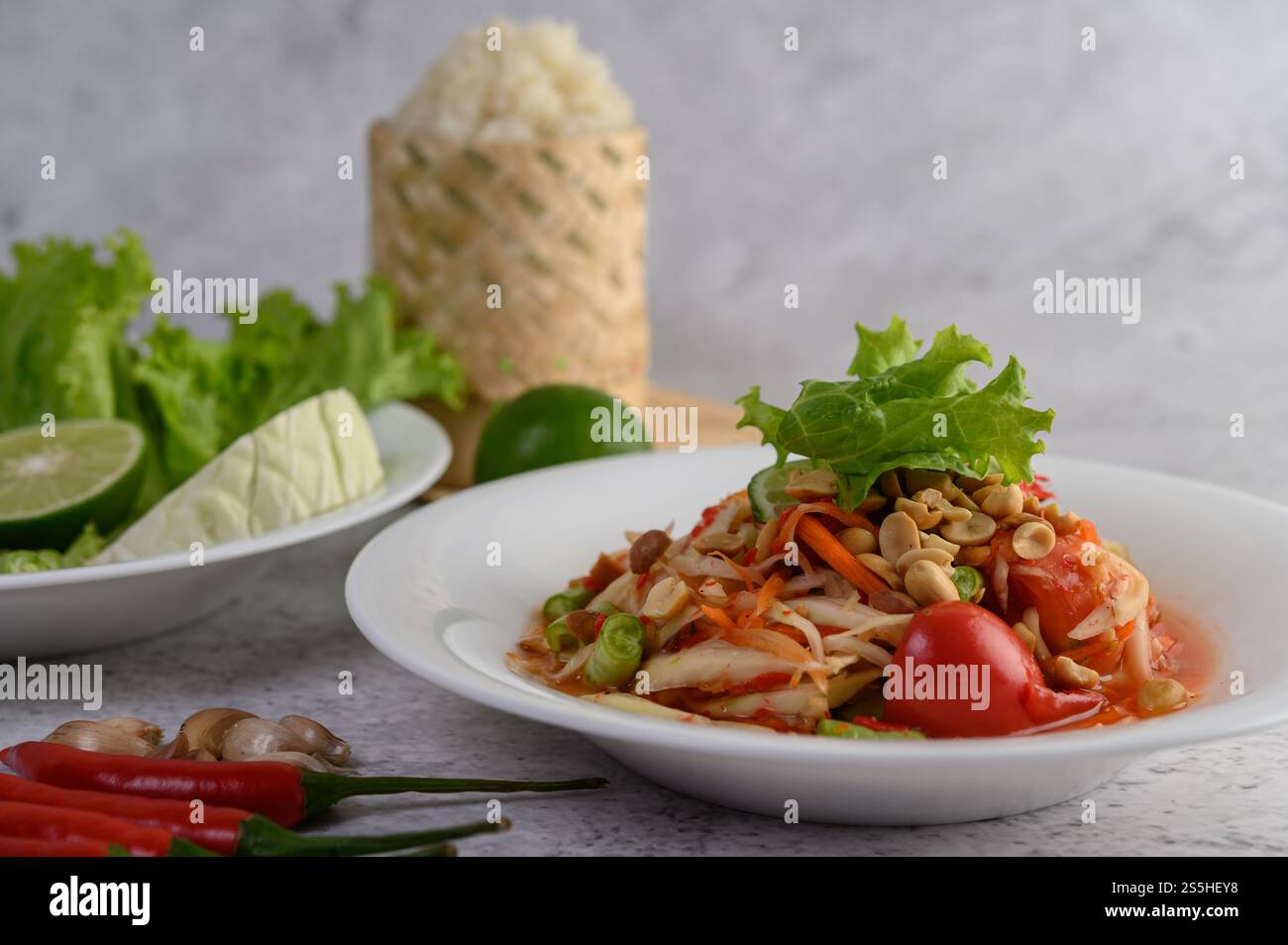 Salade de papaye thaïlandaise dans une assiette blanche avec riz collant dans un panier en osier en bambou. Banque D'Images