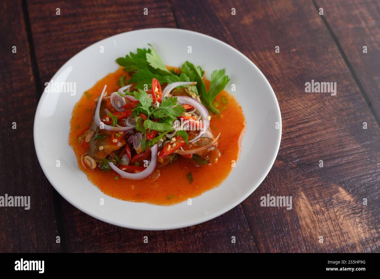 Image horizontale la salade épicée de sardine à la sauce tomate dans un plat blanc sur une table en bois, mélangée avec de l'herbe et de la limonade, copier l'espace Banque D'Images