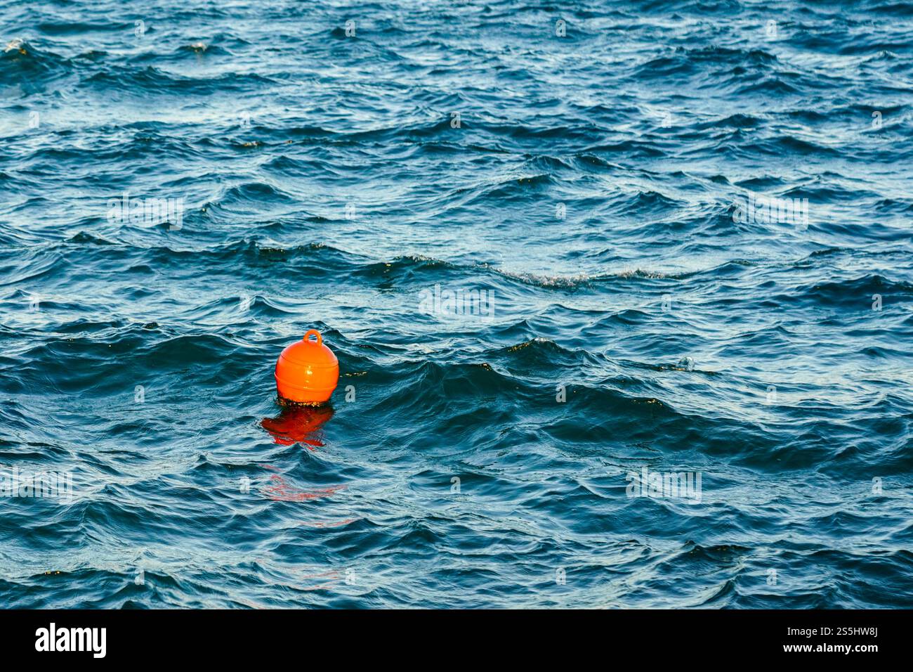 Bouée d'eau en plastique orange flottant dans l'eau de mer turquoise, fond d'eau ondulé Banque D'Images