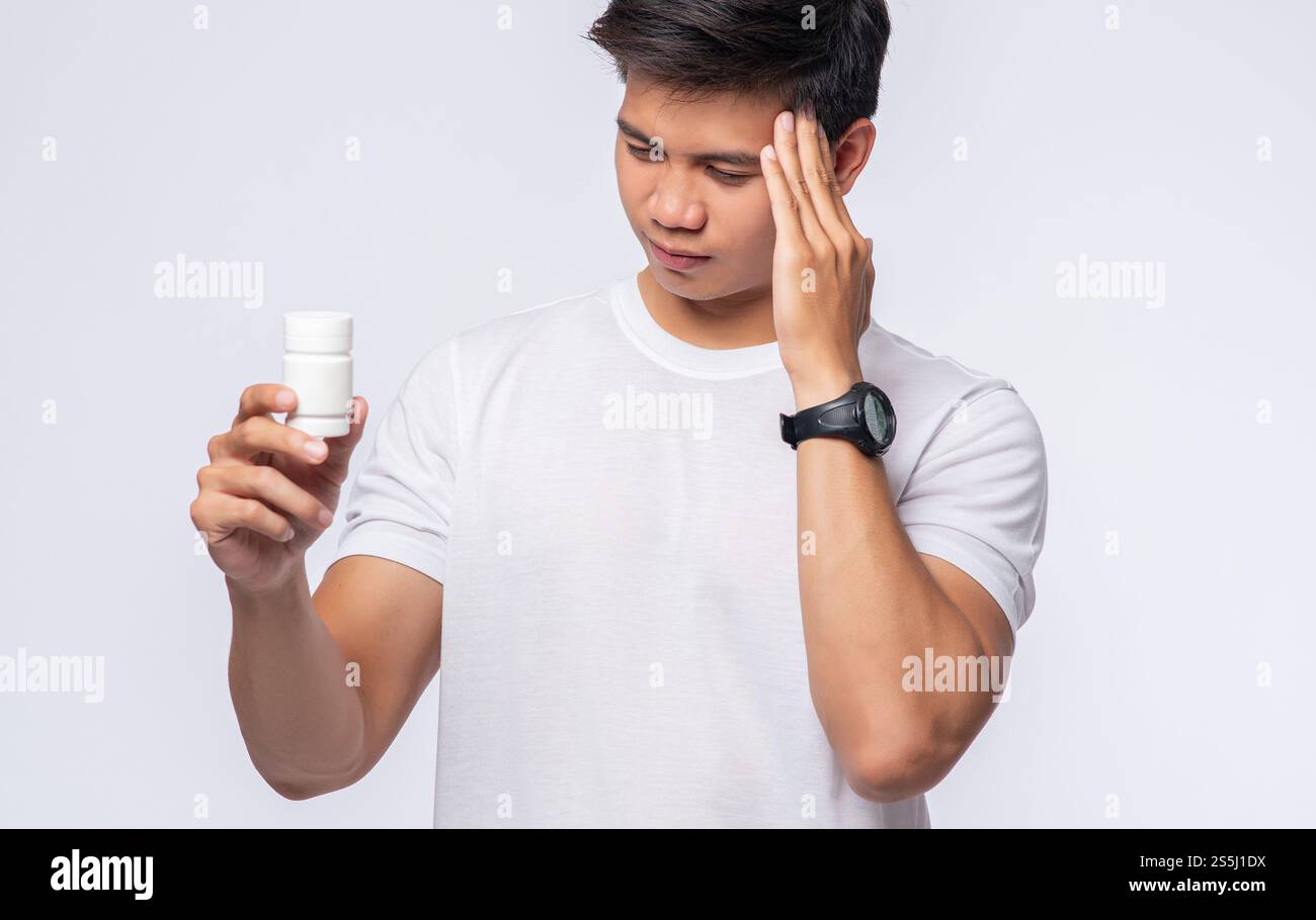 Un homme avec douleur dans sa main tient une bouteille de médicament et l'autre main mais sur sa tête Banque D'Images